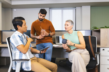Diverse coworkers discussing project ideas in open office, with tablet, coffee mug and iced coffee