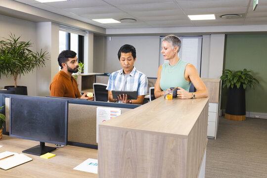 Collaborating Diverse coworkers examining tablet at modern office counter, with apple and fruit jar