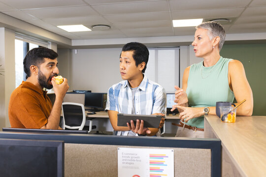 Standing Diverse coworkers snacking behind cubicle partition in office, with tablet mug and apple