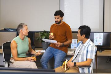 Discussing Diverse coworkers sitting in break area, holding snacks and drinks and reviewing charts