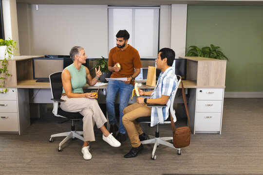 Diverse coworkers taking snack break in modern office, with bananas and orange juice