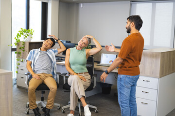 Stretching Diverse coworkers performing neck-tilt exercise at open-plan office, with laptop charts