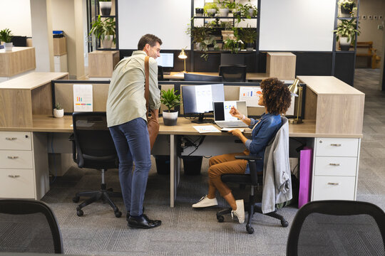 Diverse coworkers discussing chart data in modern open-plan office, with laptop and printed report - Powered by Adobe