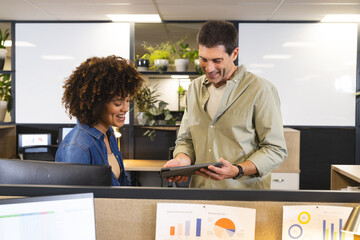 Reviewing Diverse coworkers analyzing tablet data at cubicle in modern office, with printed charts