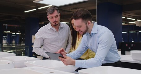 Married couple receives help from seller in plumbing store during shop visit, selecting sink for bathroom hardware needs in home, focusing on service in a professional setting with care.