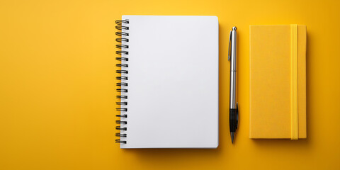 A blank notebook and a pen, with a yellow book lying beside on a yellow surface, perfect for note-taking, and journaling