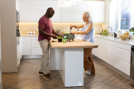 Diverse senior couple preparing salad at kitchen island, with cutting board, salad spinner