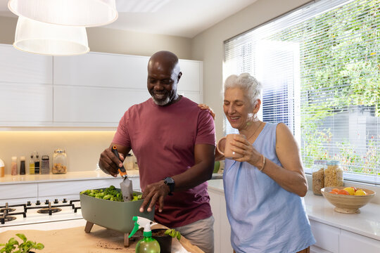Diverse couple planting seedlings in modern kitchen at island, with rectangular planter and mug