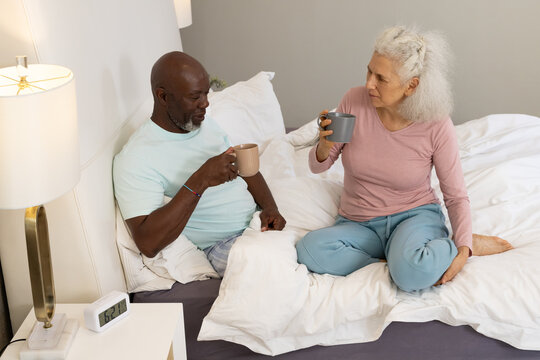 Senior couple sipping hot beverages in cozy modern bedroom on bed, with ceramic mugs - Powered by Adobe