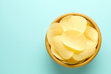 Tasty potato chips in bowl on light blue background, top view. Space for text