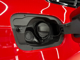 The neck of the fuel tank of a red car for refueling with gasoline fuel. An open fuel tank cap of a...