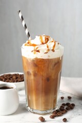 Tasty iced coffee with whipped cream, syrup and beans on white marble table