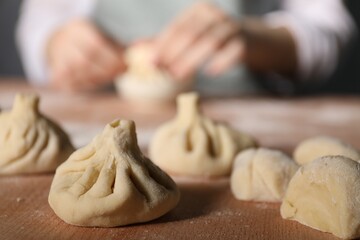 Woman making khinkali on table in kitchen, closeup