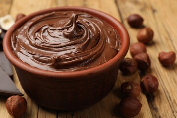 Tasty chocolate hazelnut spread and nuts on wooden table, closeup