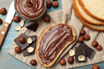 Toast with tasty hazelnut spread, chocolate pieces and nuts on blue wooden table, flat lay