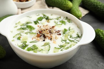 Fresh tasty cucumber soup and ingredients on black table, closeup