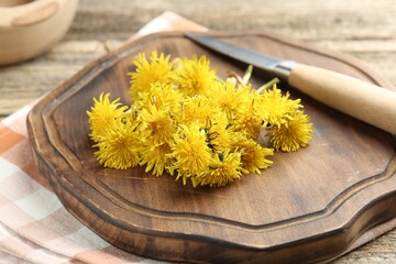Dandelion flowers, knife and cutting board on wooden table, closeup