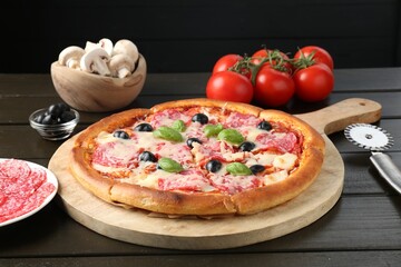 Tasty pizza, ingredients and cutter on black wooden table, closeup