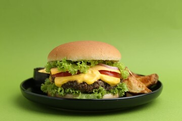 Tasty cheeseburger with sauce and potato wedges on green background, closeup