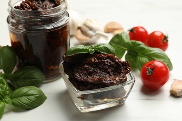 Delicious sun dried tomatoes, fresh vegetables, basil and garlic on white table, closeup