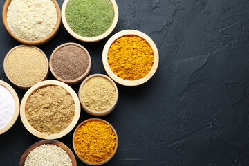 Different superfood powders in bowls on dark textured table, flat lay. Space for text