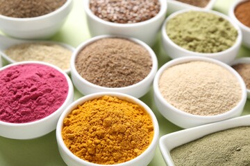Different superfood powders in bowls on pale green background, closeup