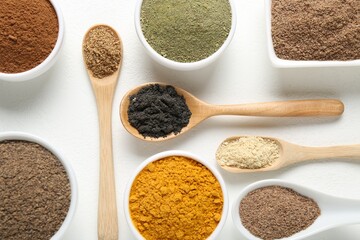 Different superfood powders in bowls and spoons on white background, flat lay
