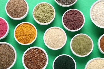 Different superfood powders in bowls on green background, flat lay