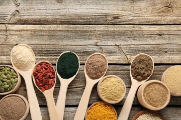Different superfoods in spoons and bowls on wooden table, flat lay. Space for text