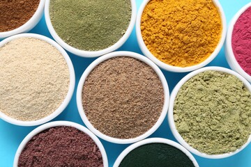 Different superfood powders in bowls on light blue background, flat lay