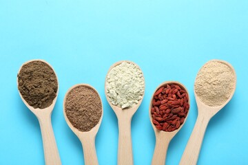 Different superfoods in spoons on light blue background, flat lay