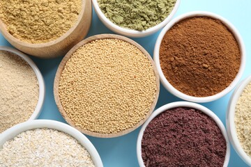Different superfood powders in bowls on light blue background, flat lay