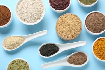 Different superfood powders in bowls and spoons on light blue background, flat lay