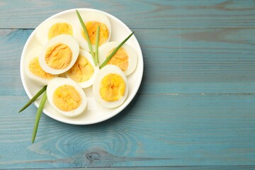 Halves of hard boiled eggs with green onions on blue wooden table, top view. Space for text