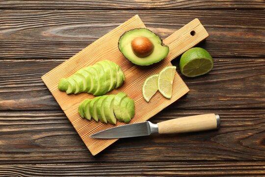 Cut ripe green avocado, lime and knife on wooden table, flat lay