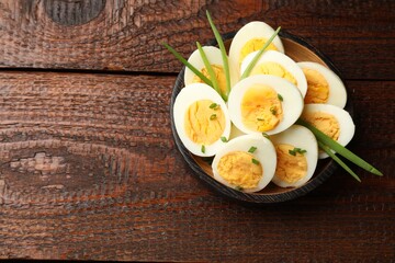 Halves of hard boiled eggs with green onions on wooden table, top view. Space for text