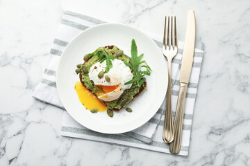 Delicious sandwich with avocado, poached egg, arugula and pumpkin served on white marble table, flat lay
