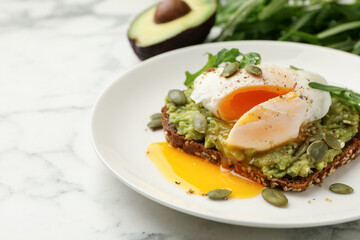 Delicious sandwich with avocado, poached egg, arugula and pumpkin on white marble table, closeup