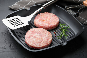 Fresh raw patties for burger and spices in frying pan on black table, closeup