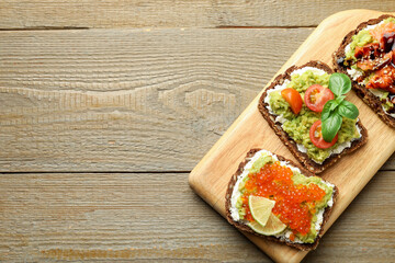 Different delicious avocado sandwiches on wooden table, top view. Space for text