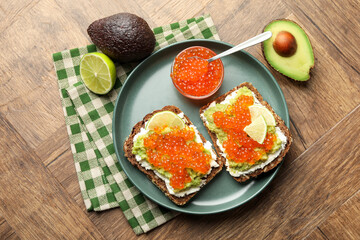 Delicious sandwiches with avocado, red caviar, cream cheese and lime on wooden table, flat lay