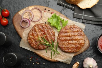 Delicious hamburger patties, tomatoes and spices on black table, flat lay