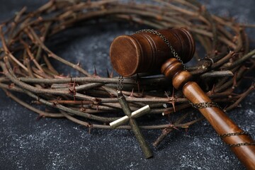 Crown of thorns and judge's gavel with cross on dark textured background, closeup