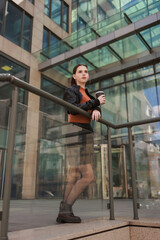 Girl with hot coffee against the background of a modern city building.