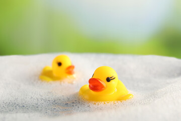 Cute rubber ducks floating in water with bubbles against blurred green background, closeup
