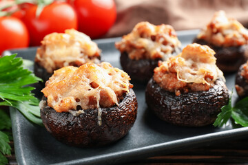 Delicious stuffed mushrooms with parsley and tomatoes on table, closeup