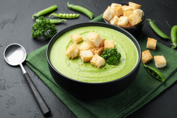 Tasty pea cream soup with croutons and broccoli served on black table, closeup