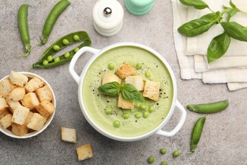 Tasty pea cream soup with croutons and basil served on grey table, flat lay
