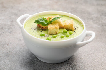 Tasty pea cream soup with croutons and basil on grey table, closeup