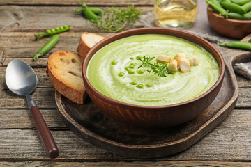 Tasty pea cream soup with croutons and thyme served on wooden table, closeup